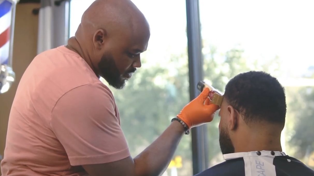 Antione Dunn cutting a client's hair by the shop window